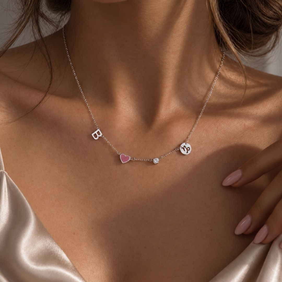Woman in a satin top wearing the silver Fable Necklace with a B initial, pink heart, stone and sign