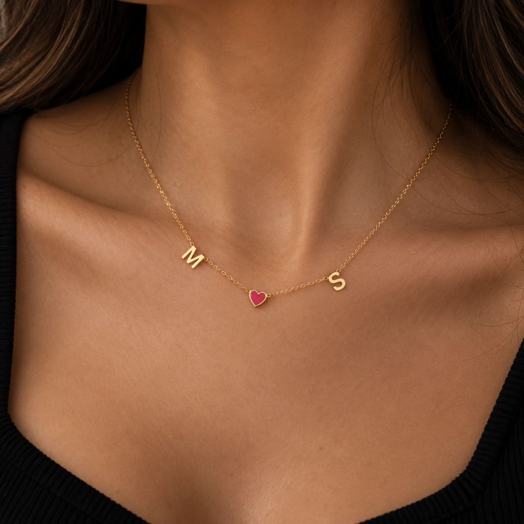 Woman wearing the gold Fable Necklace with M and S initials and a red heart charm